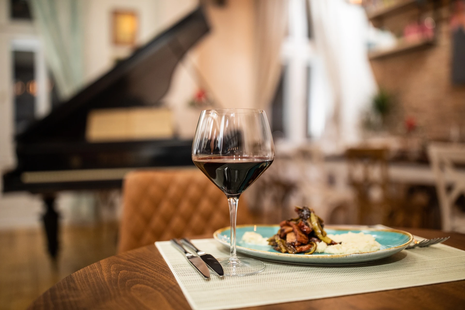 A glass of red wine beside a plate on a wooden table